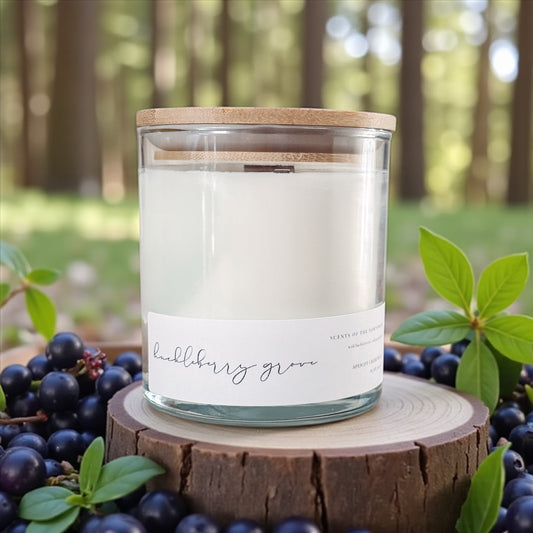 Candle in a glass jar with a wooden lid on a wooden stump surrounded by huckleberries and green leaves in a forest setting.